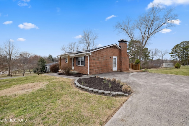 view of front of house featuring driveway, brick siding, a chimney, and a front yard