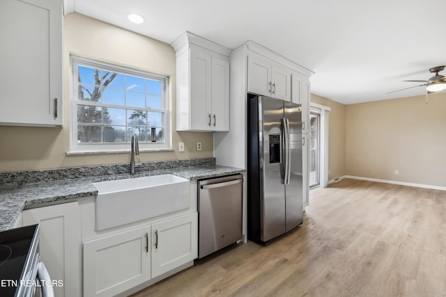 kitchen featuring light stone counters, stainless steel appliances, a sink, white cabinetry, and light wood finished floors