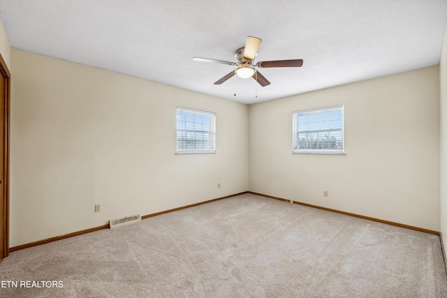 carpeted empty room featuring a textured ceiling, ceiling fan, visible vents, and baseboards