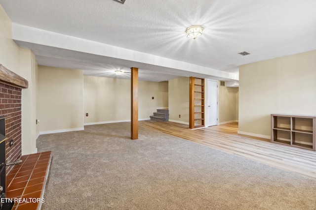 finished basement with carpet floors, a fireplace, visible vents, a textured ceiling, and stairs