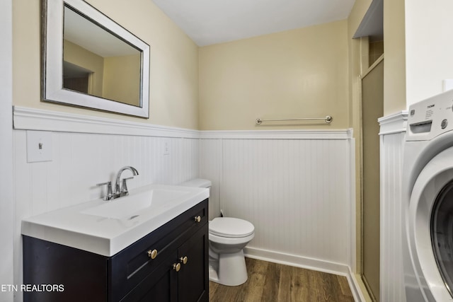 bathroom with washer / dryer, toilet, a wainscoted wall, wood finished floors, and vanity