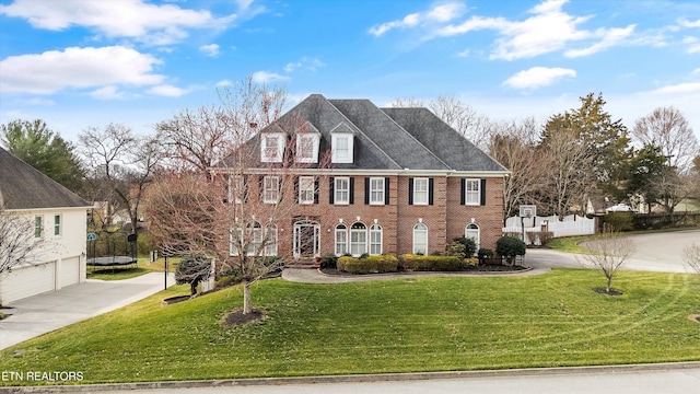 colonial inspired home featuring brick siding, driveway, a front lawn, and a trampoline