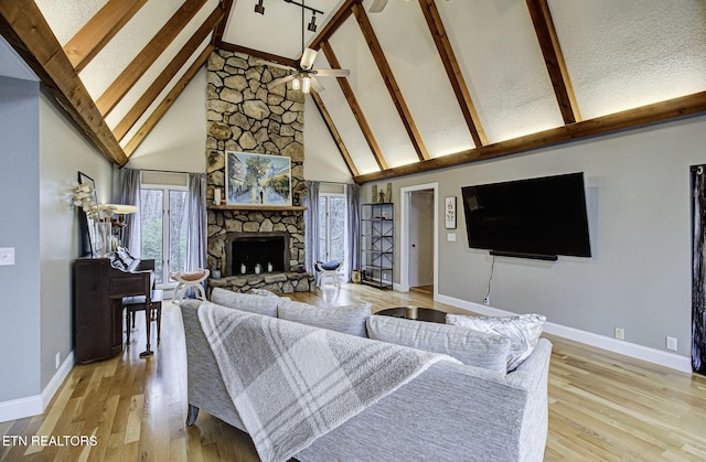 living room featuring beam ceiling, a stone fireplace, high vaulted ceiling, and light wood-style floors