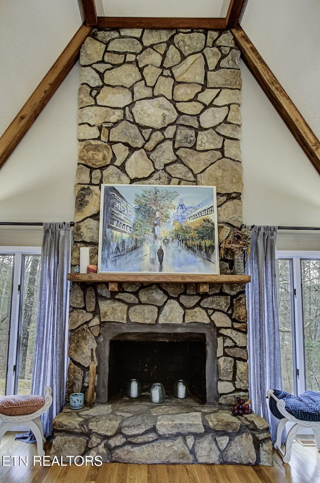 details featuring beam ceiling, a stone fireplace, and wood finished floors