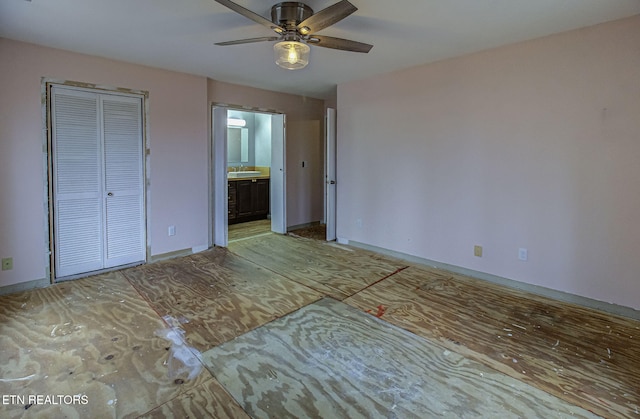 unfurnished bedroom featuring baseboards, ensuite bath, ceiling fan, a sink, and a closet