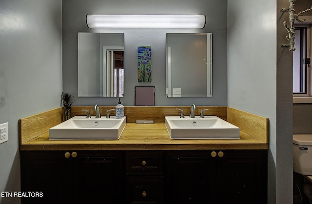 bathroom featuring double vanity, toilet, and a sink