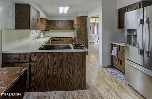 kitchen with light wood-style flooring, a sink, a peninsula, appliances with stainless steel finishes, and light countertops