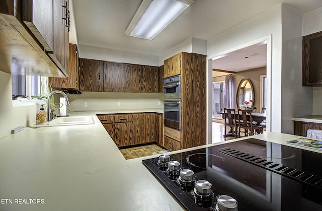 kitchen with a sink, black electric cooktop, stainless steel double oven, and light countertops