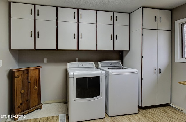 washroom with visible vents, light wood-style flooring, cabinet space, a textured ceiling, and washing machine and dryer