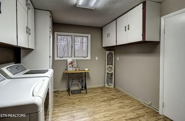 laundry area featuring baseboards, washing machine and dryer, light wood-style floors, cabinet space, and a textured ceiling