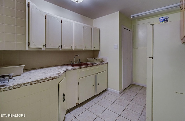 kitchen featuring light tile patterned floors, freestanding refrigerator, a sink, light countertops, and backsplash