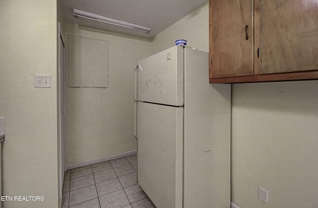 kitchen featuring light tile patterned flooring, baseboards, freestanding refrigerator, and brown cabinets