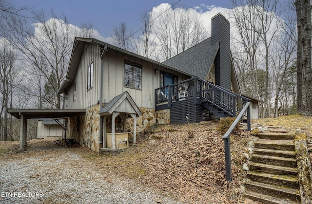 view of side of property with stone siding, stairway, a shingled roof, an attached carport, and a chimney