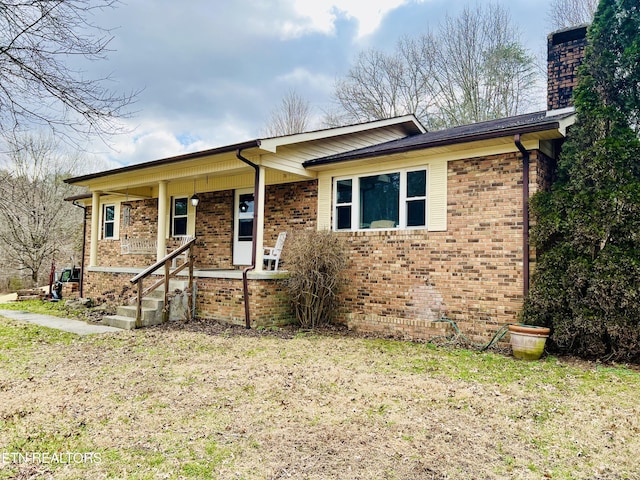 ranch-style home featuring covered porch, brick siding, a chimney, and a front lawn