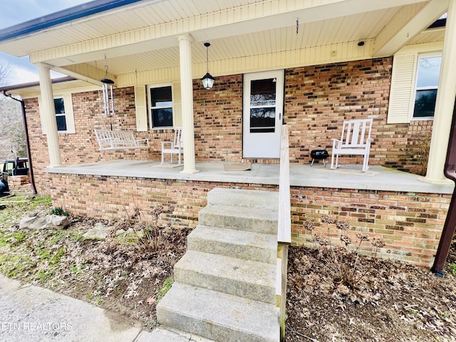 entrance to property with covered porch and brick siding