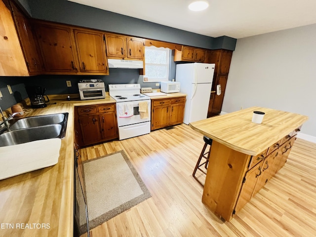 kitchen with under cabinet range hood, white appliances, a sink, light countertops, and light wood finished floors