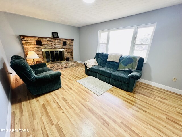 living room with a brick fireplace, baseboards, and wood finished floors