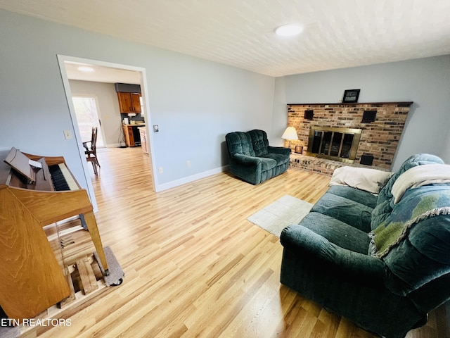 living area featuring a brick fireplace, light wood-type flooring, and baseboards