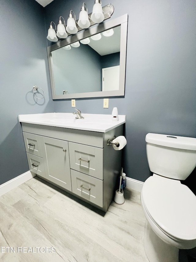 bathroom with toilet, baseboards, wood finished floors, and vanity