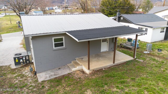 exterior space with metal roof, a patio, a lawn, and concrete block siding