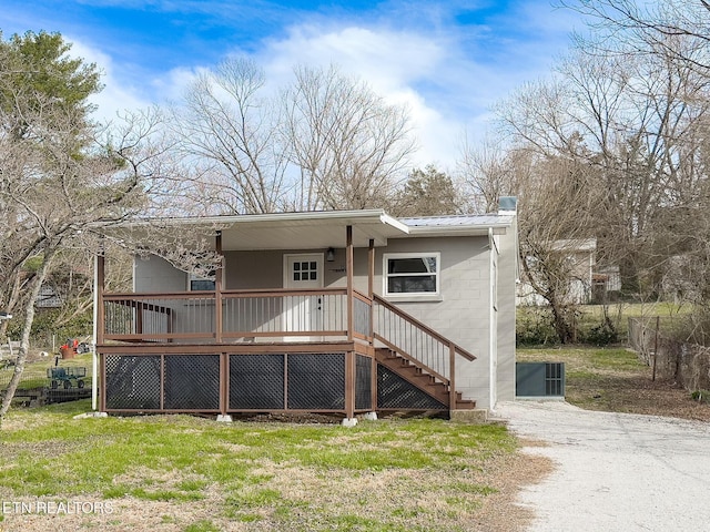 rear view of property featuring metal roof, concrete block siding, stairs, driveway, and a chimney