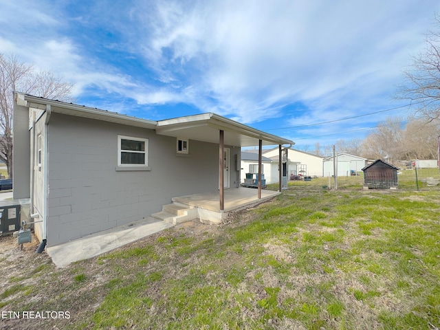 rear view of property with concrete block siding, a patio area, and a lawn