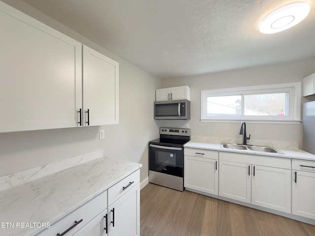 kitchen featuring appliances with stainless steel finishes, white cabinetry, a sink, light stone countertops, and light wood-type flooring