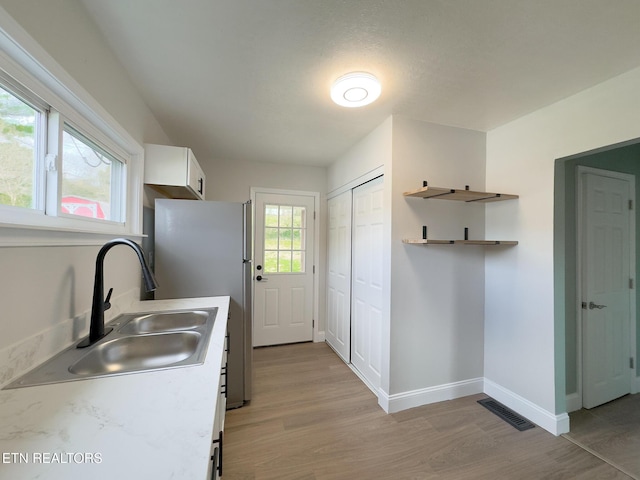 kitchen featuring baseboards, white cabinets, light countertops, light wood-type flooring, and a sink