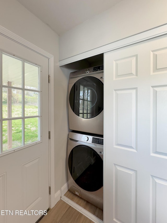 clothes washing area with wood finished floors, stacked washer and clothes dryer, baseboards, and laundry area