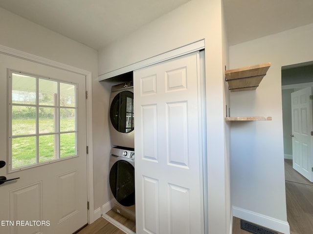 clothes washing area featuring stacked washing maching and dryer, baseboards, laundry area, and visible vents