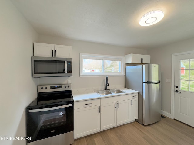 kitchen with light wood-style flooring, stainless steel appliances, a sink, white cabinetry, and light countertops