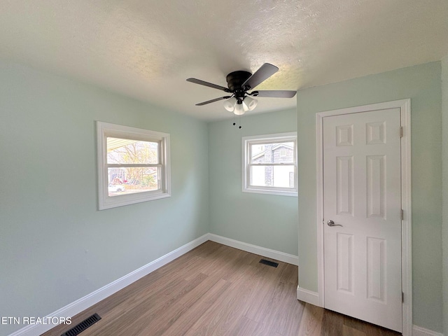 unfurnished bedroom featuring baseboards, a textured ceiling, visible vents, and wood finished floors