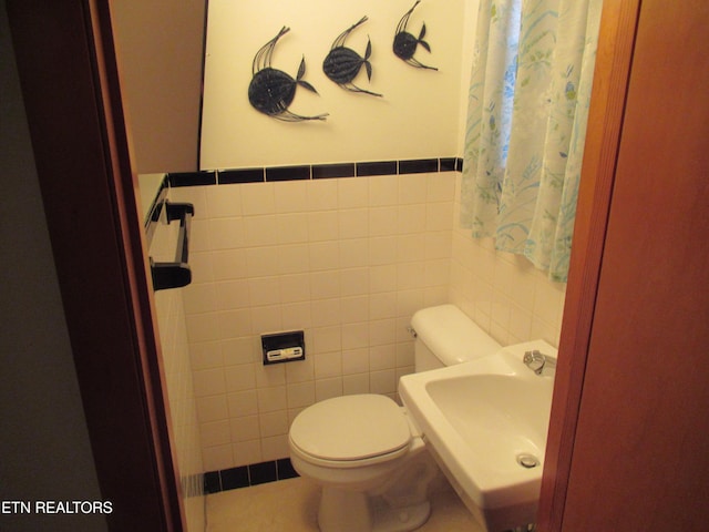 half bathroom featuring wainscoting, a sink, toilet, and tile walls