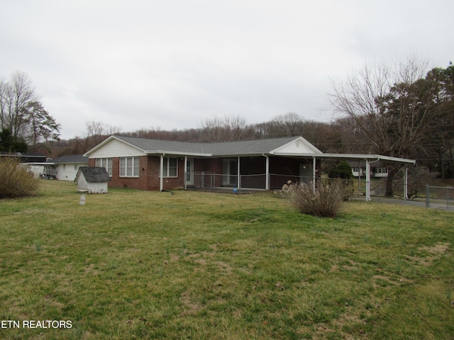 view of front of property with an outbuilding, brick siding, fence, an attached carport, and a front lawn