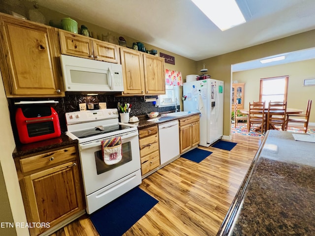 kitchen featuring dark countertops, backsplash, white appliances, and light wood-type flooring