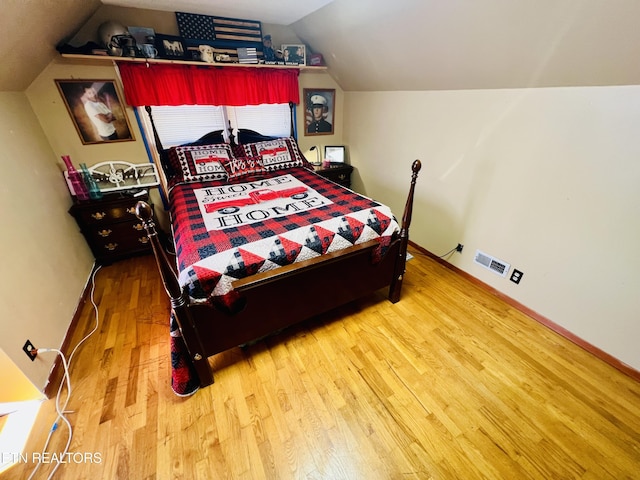 bedroom featuring visible vents, baseboards, wood finished floors, and vaulted ceiling