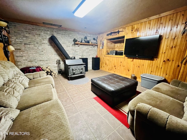 living area with a wood stove, light tile patterned floors, wooden walls, and brick wall