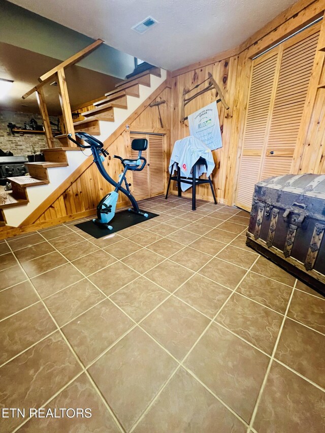 exercise room with visible vents, wood walls, and tile patterned flooring