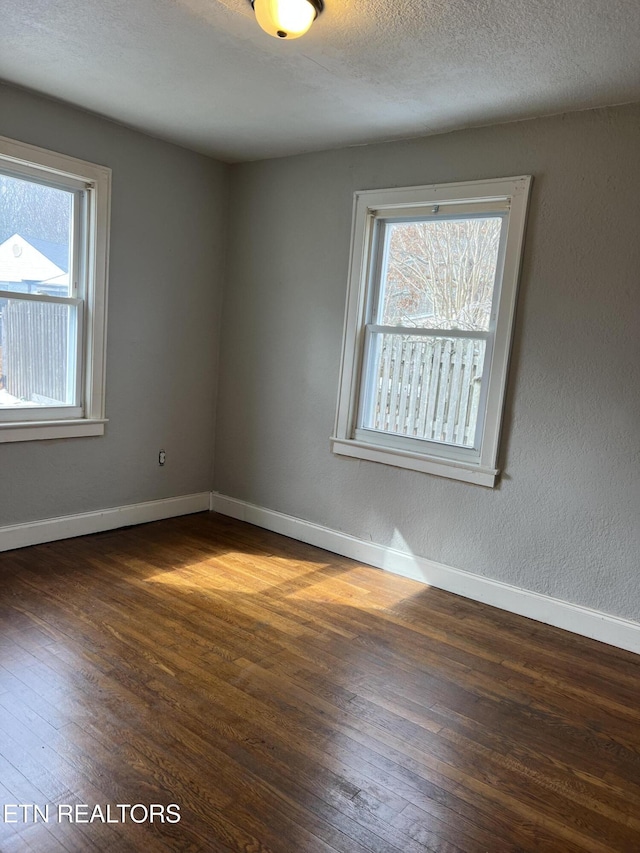 unfurnished room with a textured ceiling, dark wood-type flooring, baseboards, and a textured wall