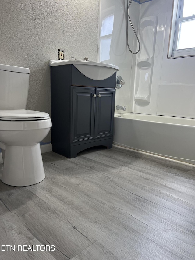 bathroom featuring toilet, wood finished floors, shower / bath combination, vanity, and a textured wall