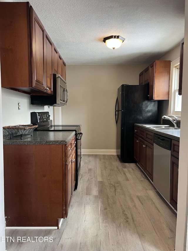 kitchen featuring light wood-type flooring, black appliances, a sink, dark countertops, and a textured ceiling