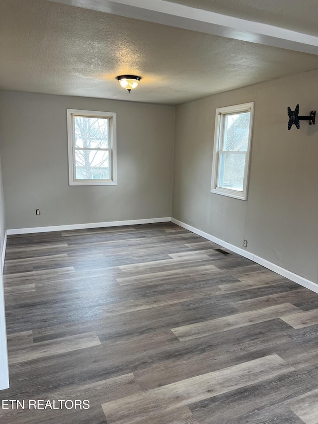 spare room with plenty of natural light, a textured ceiling, and dark wood-type flooring