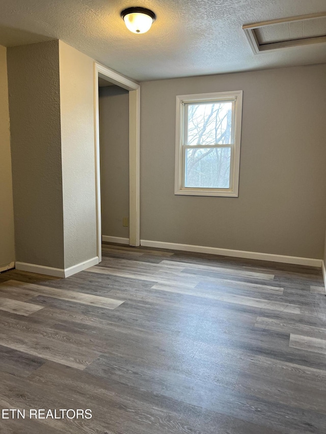 unfurnished room featuring attic access, a textured ceiling, baseboards, and wood finished floors