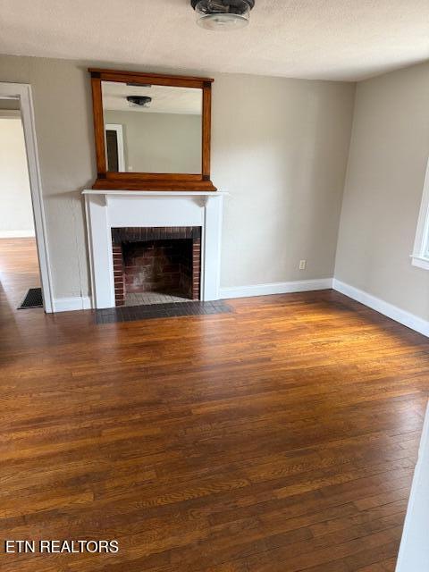 unfurnished living room with visible vents, baseboards, a fireplace, wood finished floors, and a textured ceiling