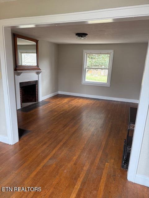 unfurnished living room with visible vents, baseboards, dark wood-type flooring, and a fireplace