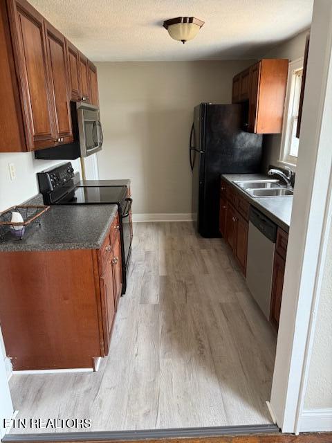 kitchen with a sink, a textured ceiling, black appliances, and brown cabinetry