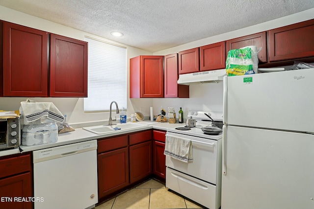 kitchen with reddish brown cabinets, under cabinet range hood, light tile patterned floors, white appliances, and a sink