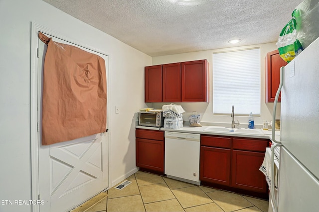 kitchen with light tile patterned flooring, dark brown cabinets, white appliances, and a sink