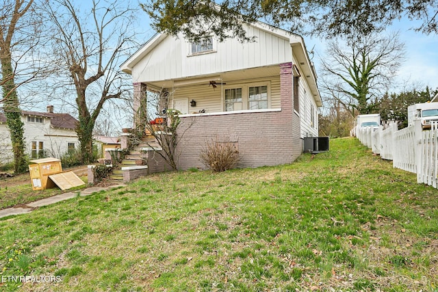 view of front of property featuring fence, stairs, a front yard, covered porch, and central AC unit