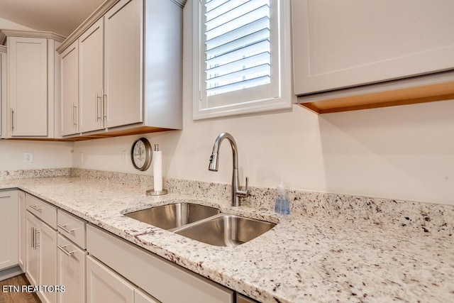 kitchen with a sink, light stone countertops, and wood finished floors